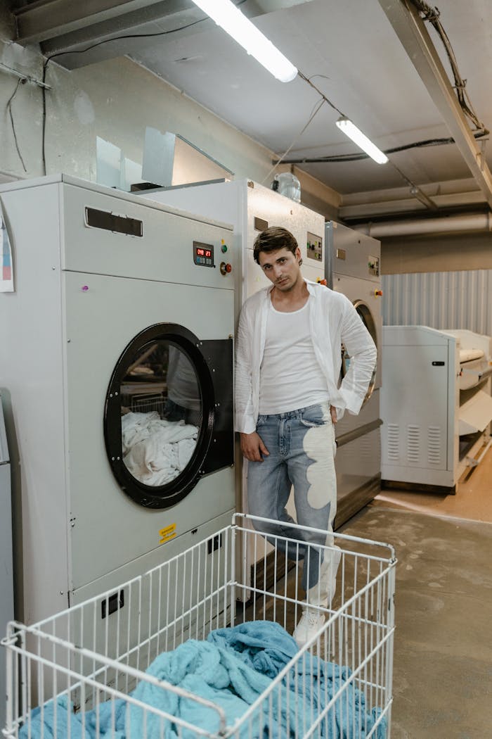 Casual man standing by industrial dryers in a laundromat.